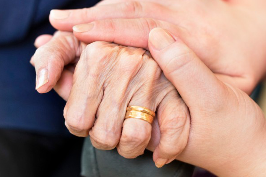 Bild på två par händer. En yngre persons händer håller i en äldre persons hand.