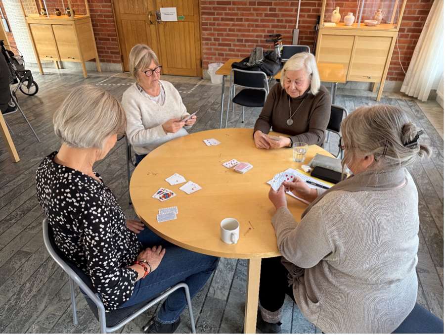 Seniorer sitter vid ett bord och spelar kort.