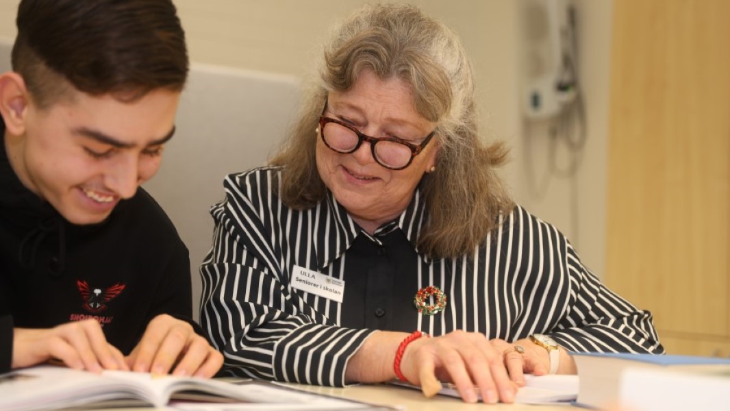 Ung kille får hjälp av äldre dam vid ett skrivbord.