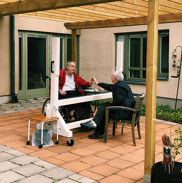 Man och kvinna high-fivear genom plexiglasrutan.