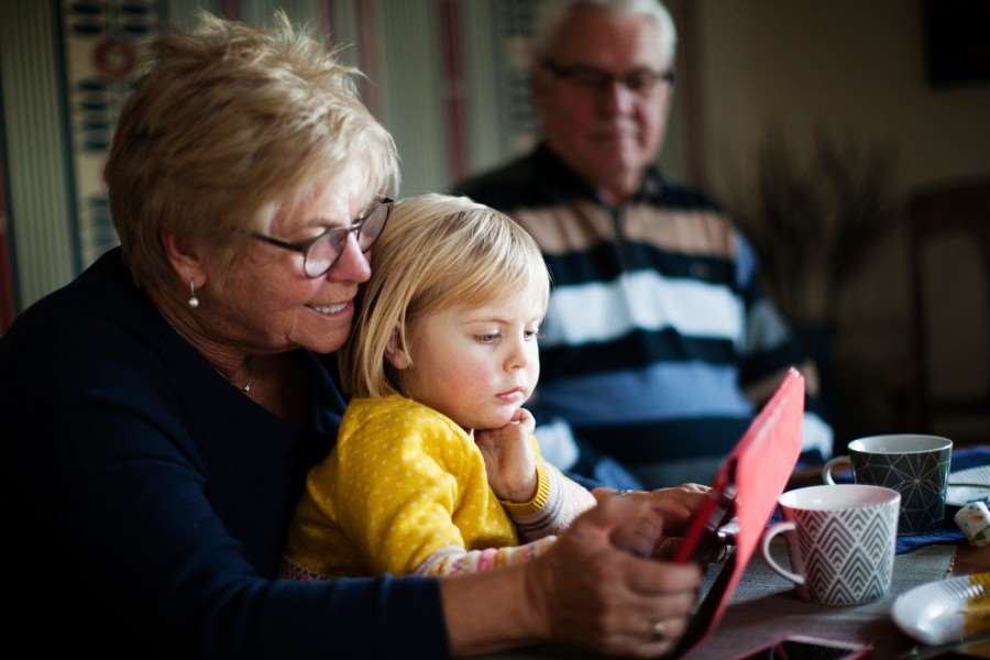 Mormor och morfar tillsammans med barnbarn. De fikar och svarar på enkäten på en surfplatta.