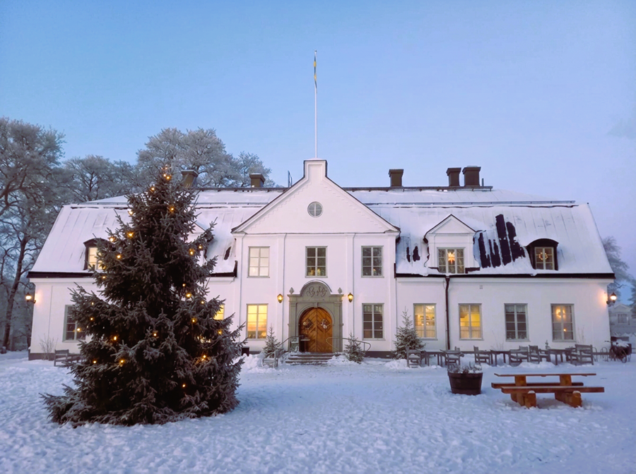 Vit herrgårdsbyggnad med en julgran framför