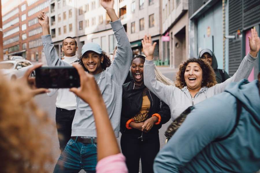Tjej som fotograferar glada vänner som dansar med en smartphone i staden.