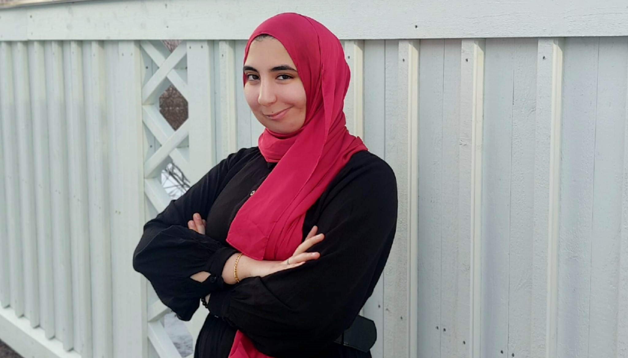 En person står och tittar in i kameran. Personen ser glad ut.