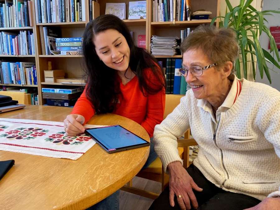 En ung glad kvinna hjälper en äldre kvinna med en Ipad.