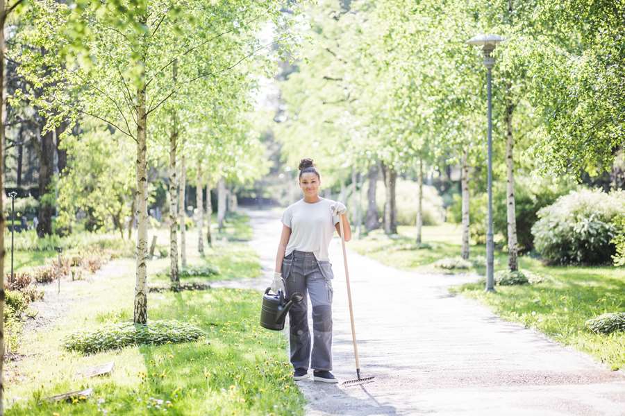 Ung kvinna med trädgårdsredskap i parkmiljö.