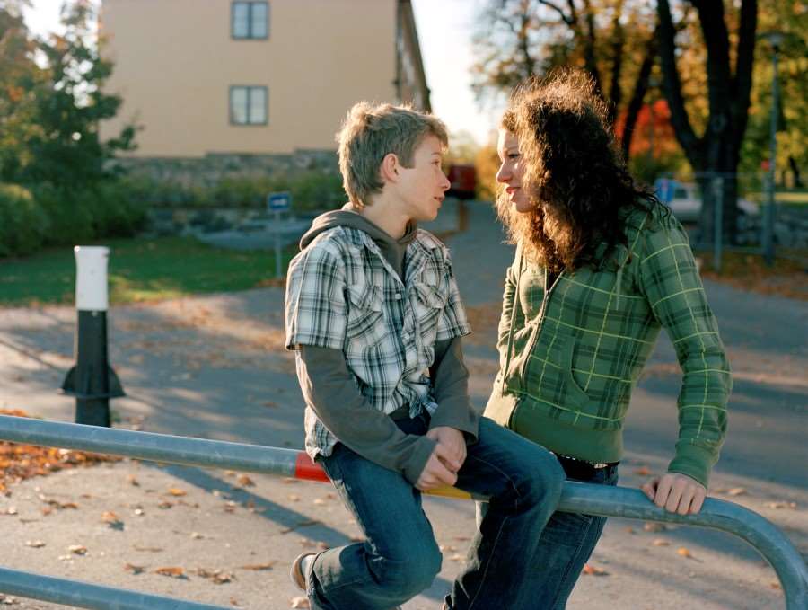 Två personer står vid ett staket och pratar med varandra.