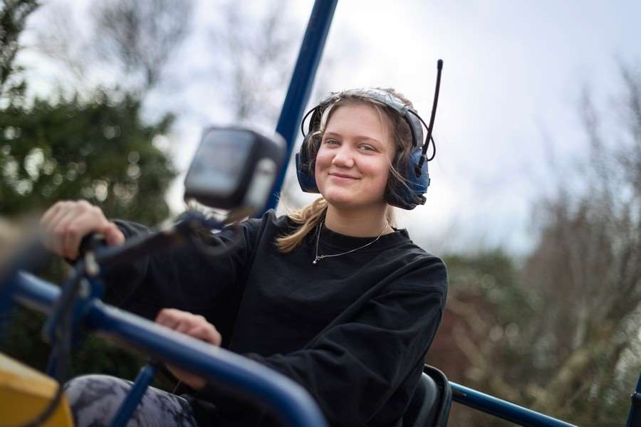 Ung tjej med hörselkåpor kör en traktor.