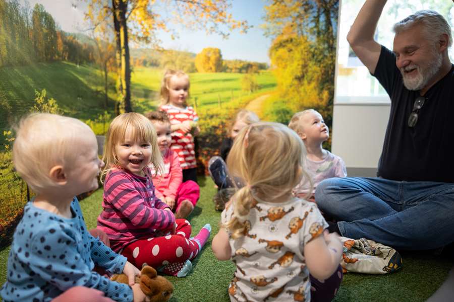 Förskolebarn ler och skrattar tillsammans med en förskollärare.