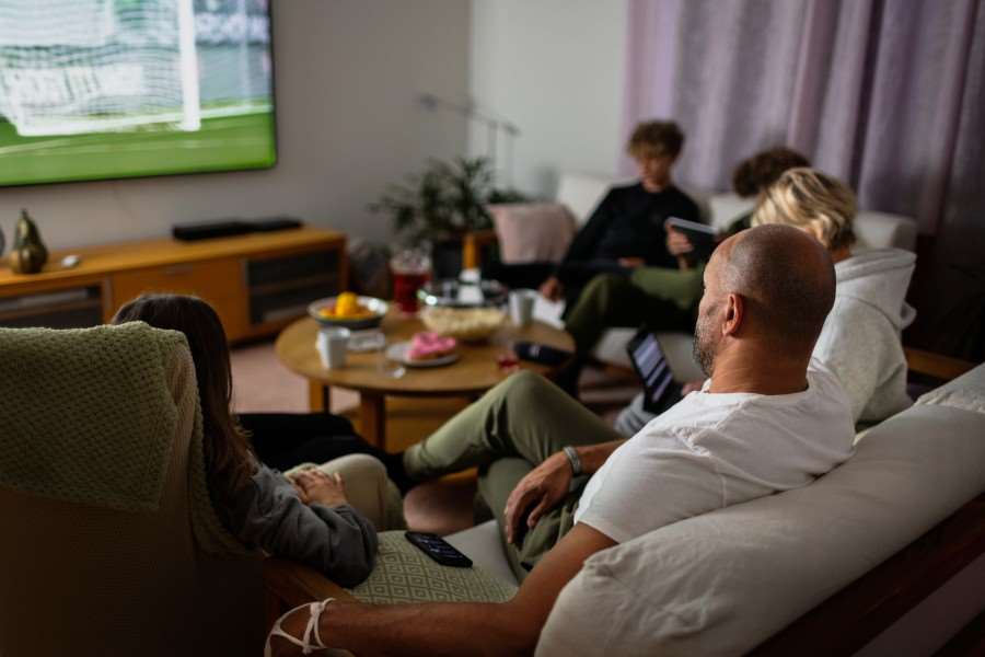 En familj sitter i en soffa och tittar på fotboll tillsammans.