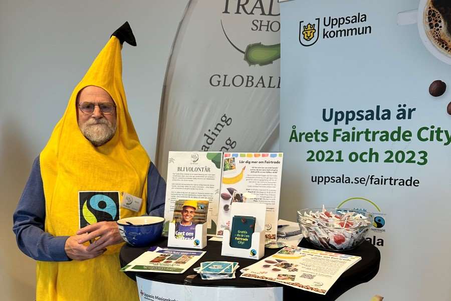 En person står iklädd en banandräkt vid ett ståbord med olika informationsmaterial på som handlar om Fairtrade.