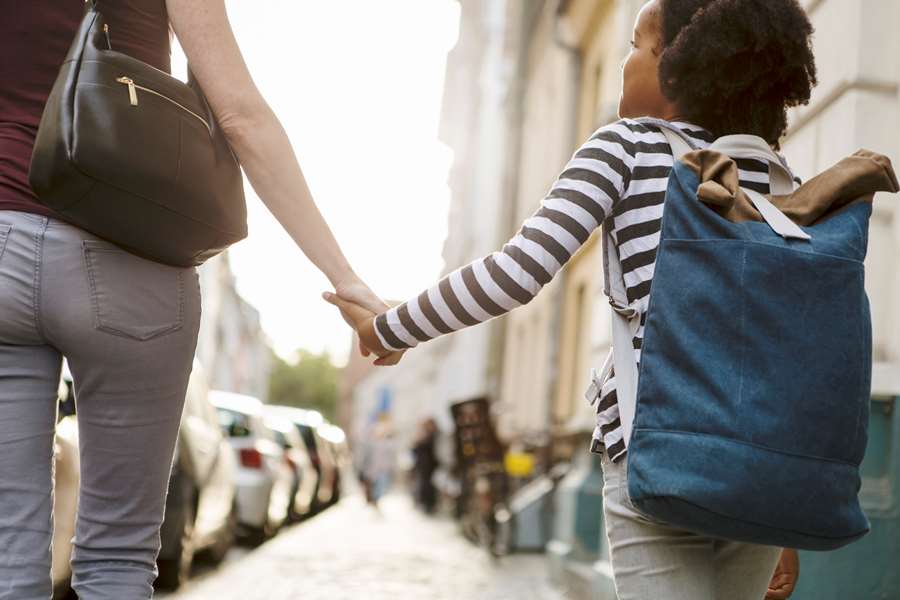 Kvinna håller handen på ett barn med ryggsäck