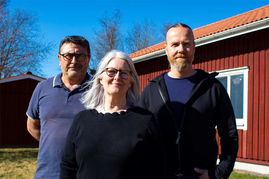 Två män och en kvinna står utanför ett hus