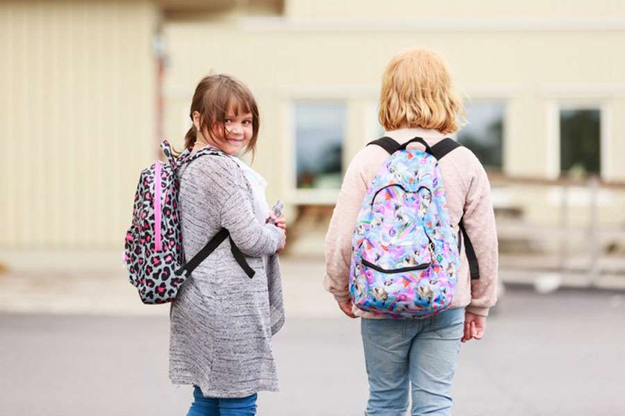 Två unga elever med ryggsäck på väg in på en skola
