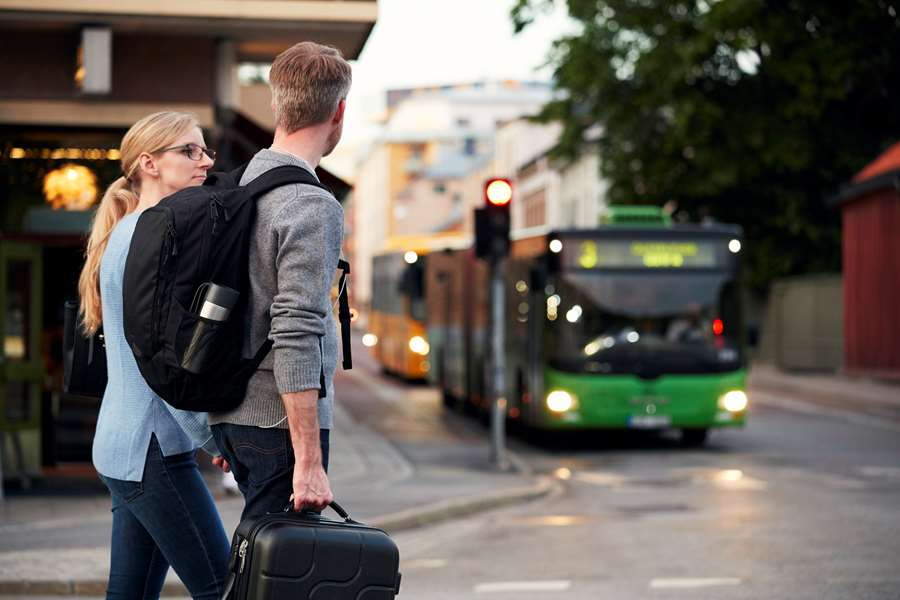 Två personer går över ett övergångsställe. En grön buss syns i bakgrunden.