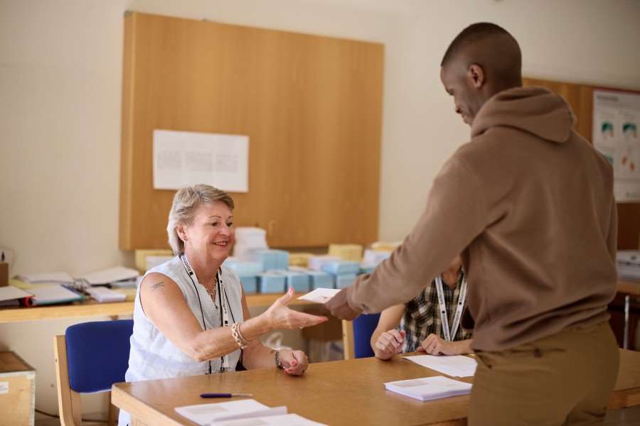 En person lämnar fram sin röst till en person som jobbar som röstmottagare som sitter bakom ett bord.