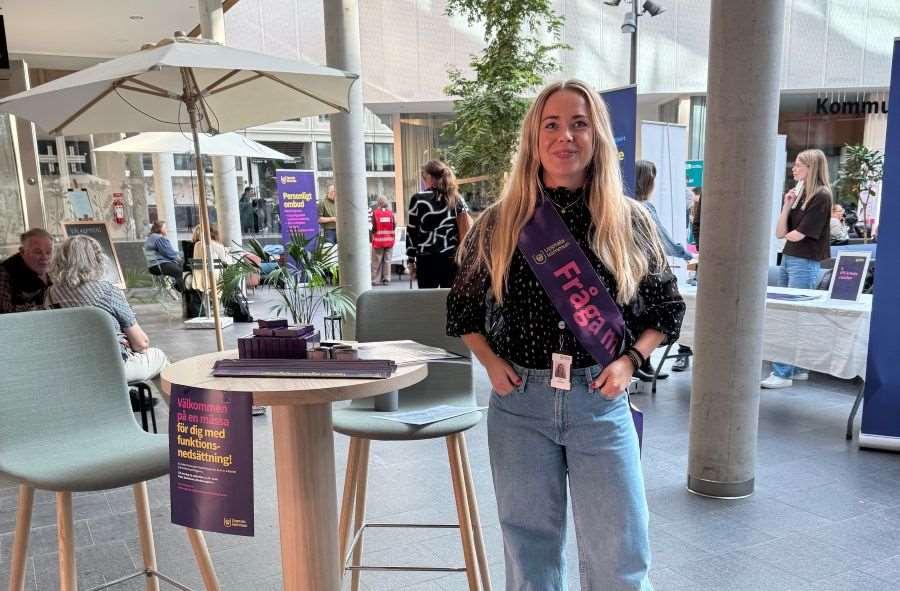 En kvinna står i Stadshuset med broschyrer, fråga mig-band.