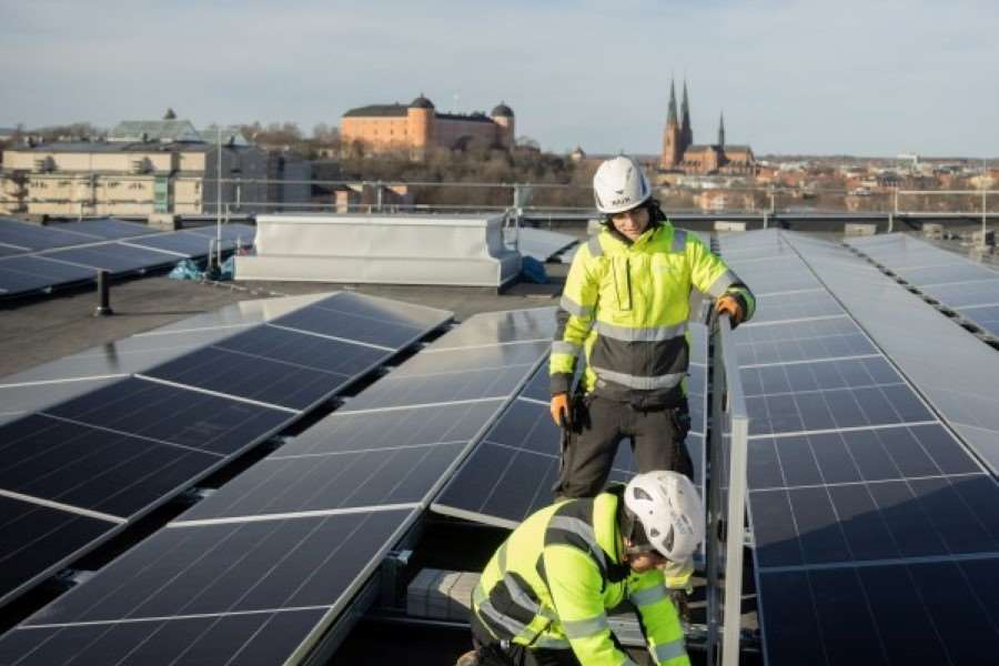 Två personer som installerar solceller på ett tag. I bakgrunden syns Uppsala slott och domkyrkan.