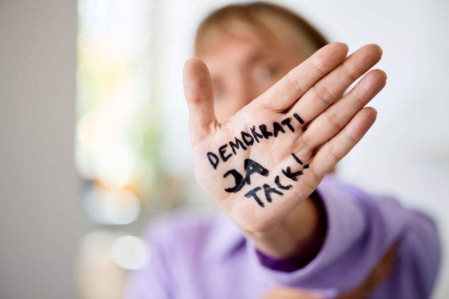 En person med en hand utsträckt mot kameran. I handen står det Demokrati Ja tack