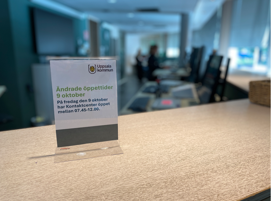 Skylt på en receptionsdisk med information om särskilda öppettider 9 oktober. I bakgrunden ser man personal i oskärpa.