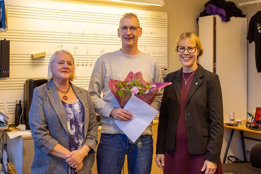 Tre personer står i ett klassrum och kollar mot kameran