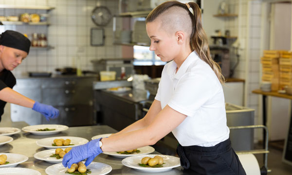 Tjej lägger upp mat på tallrik i restaurangkök