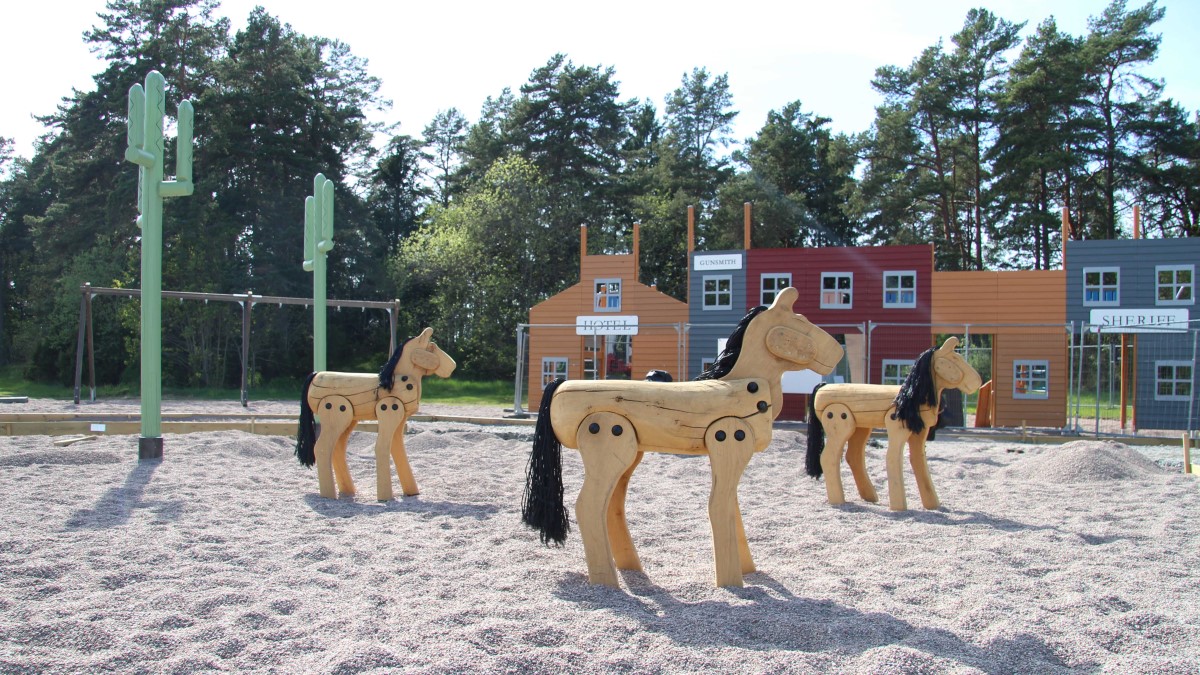 Lekplats med sand, hästar och kaktusar i trä och västernfasader.