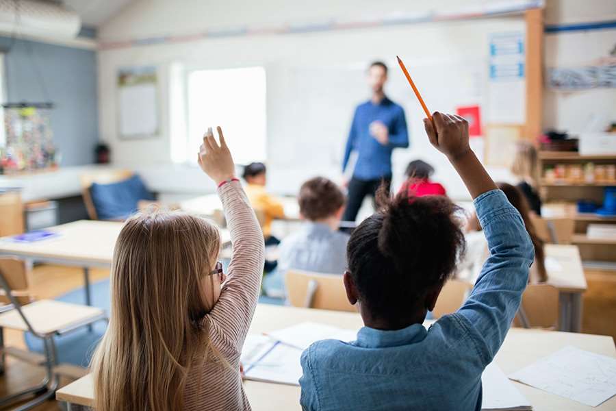 Interiörbild från ett klassrum. Två elever räcker upp handen.