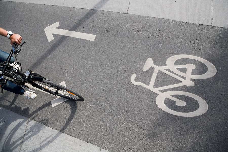 Bild tagen uppifrån på en cykelbana med en markering på asflten om vilken riktning cyklister ska köra. I bilden syns även en cyklist