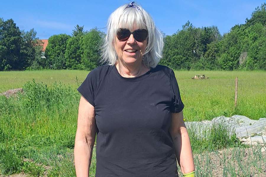 Kvinna i svart t-shirt står i ett trädgårdsland