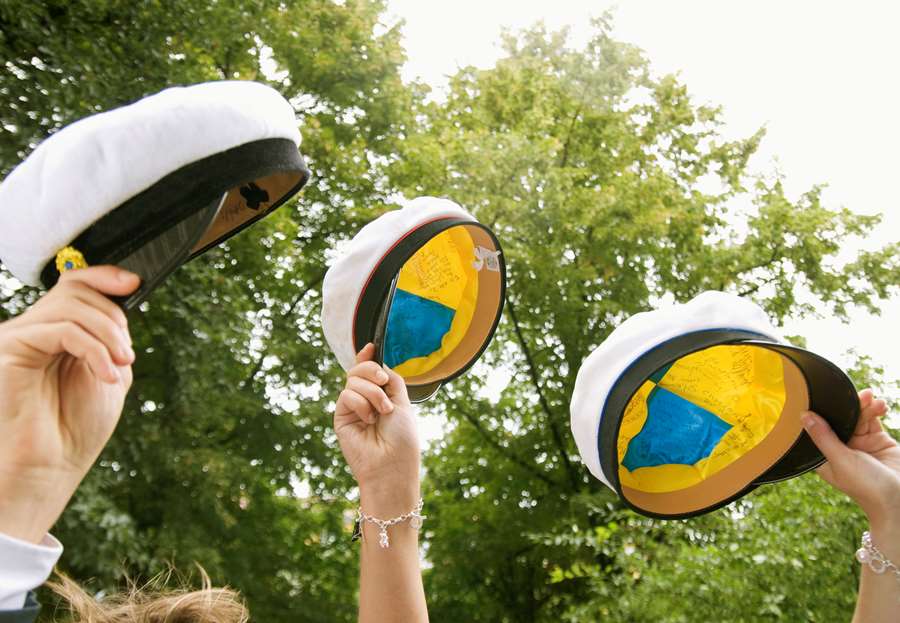 Tre studentmössor som hålls upp mot himlen