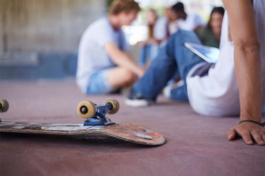 Några ungdomar sitter på marken, en uppochnedvänd skateboard syns i förgrunden