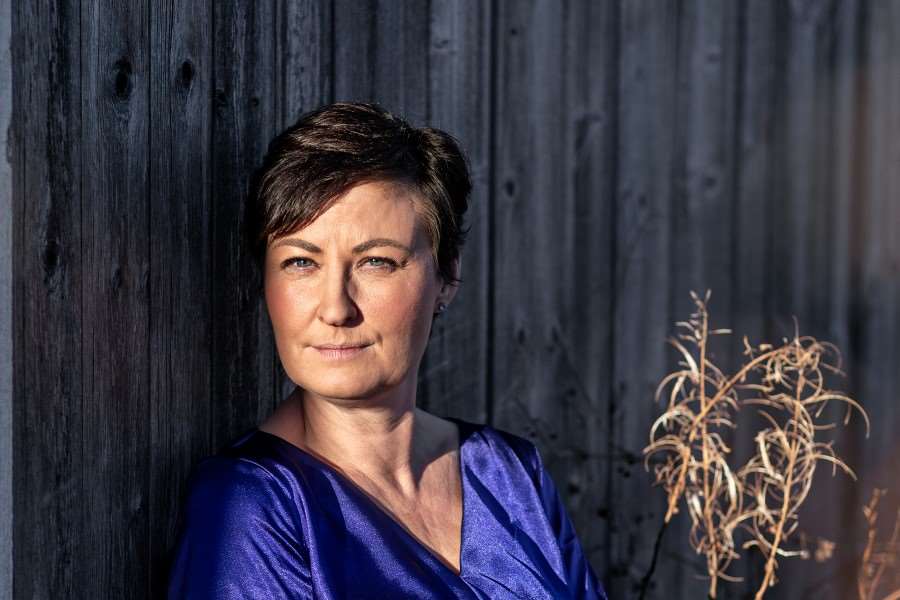 Porträttbild Sandra Jönsson - står lutad mot en grå vägg