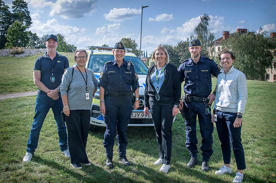 Sex personer står på rad i en park. Ett par personer har polisuniform på sig.