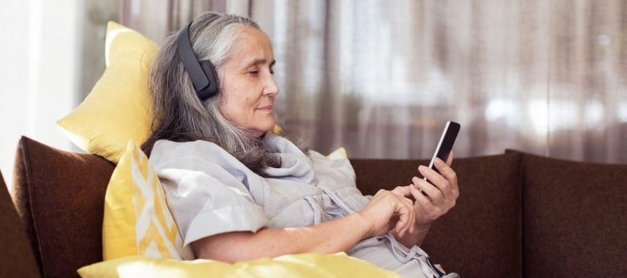 Äldre kvinna med hörlurar kopplade till mobilen