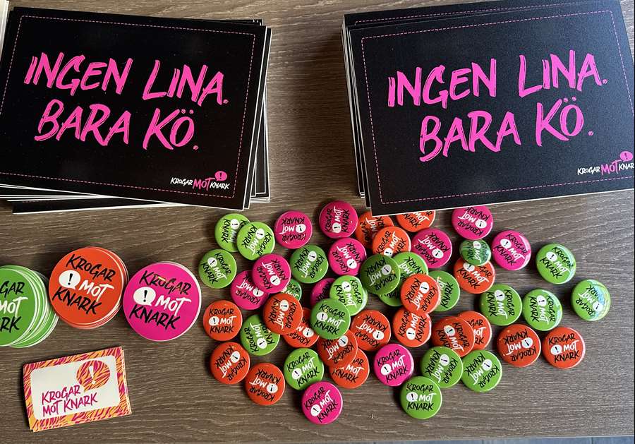 Bord med kampanjmaterial från ”Krogar mot knark”, inklusive två svarta skyltar med texten ”Ingen lina. Bara kö.” och många färgglada knappar med kampanjens logotyp.