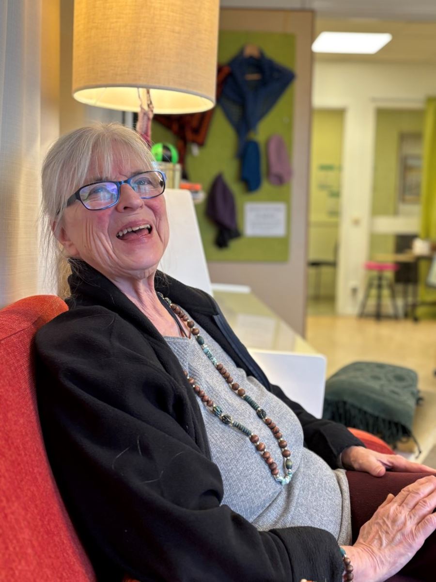 En kvinna sitter i en soffa och ler in i kameran