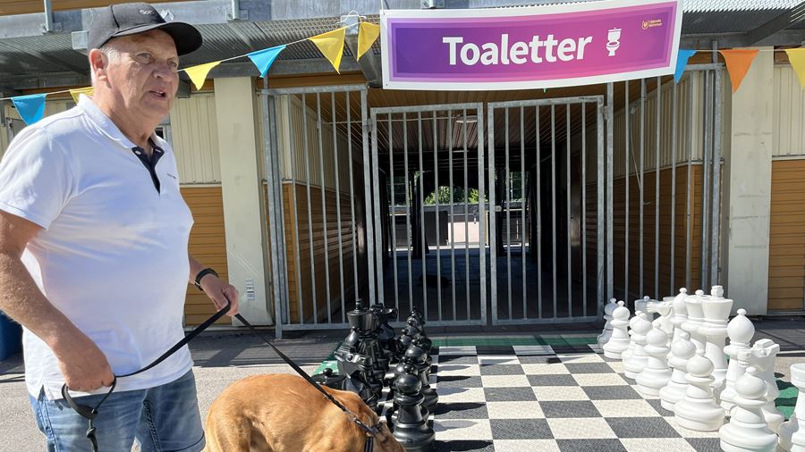 En hund nosar på ett schack i storformat, en man håller i kopplet