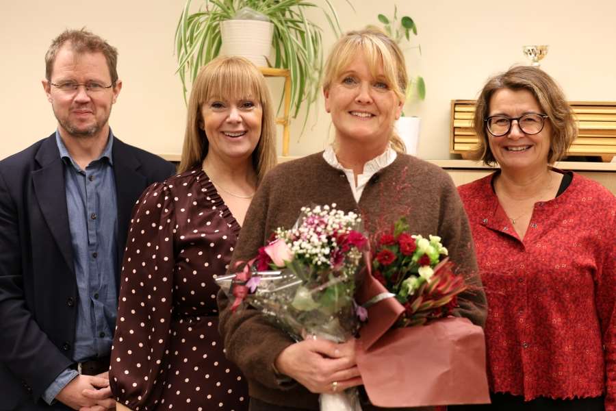 Fyra personer ler mot fotografen, en person har en bukett blommor i handen.