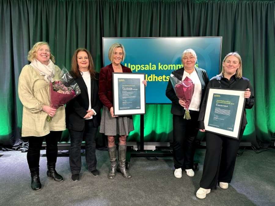 Fem kvinnor står mot grön vägg och håller i två diplom