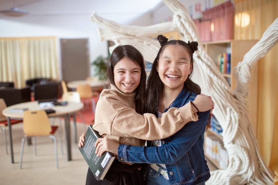Två glada flickor håller om varandra och en av dem håller i en bok