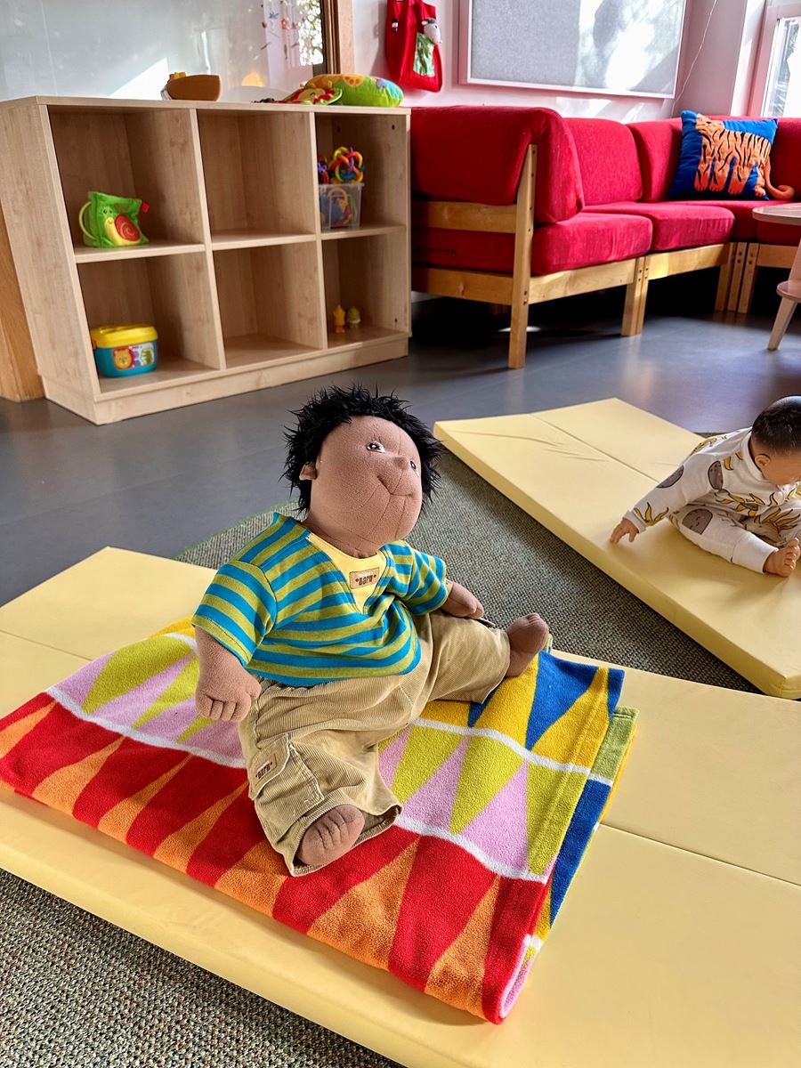 En tygdocka sitter på en liten madrass på golvet på en förskola.