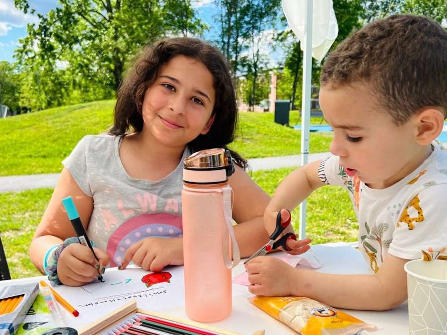 Två barn sitter vid ett bord i en park och ritar