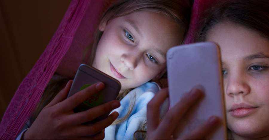 Två unga tjejer sitter bredvid varandra och tittar på sina mobiltelefoner. Foto: www.johner.se/Elliot Elliot