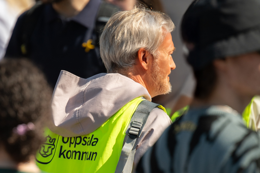 En äldre man har en gul reflexväst med en uppsala kommun-logga på ryggen. Runtom mannen är det många människor som är oskarpa i bilden. Foto av Cosmin Ignat