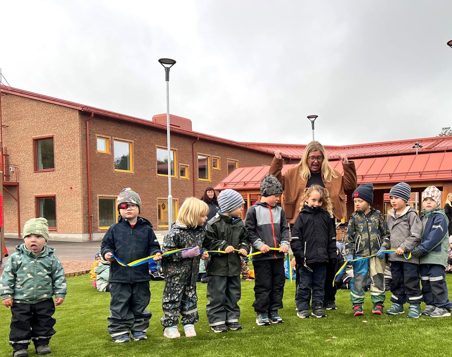 Förskolebarn i vinterkläder klipper band på ingivning.