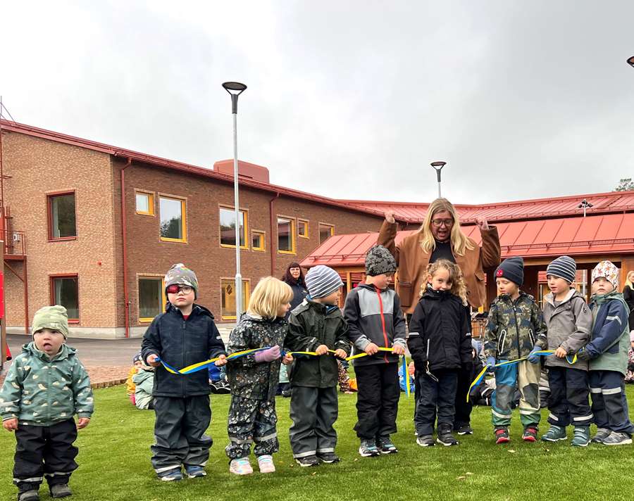 Förskolebarn i vinterkläder klipper band på ingivning.