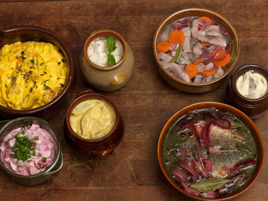 Ett julbord med flera krus med olika sillsorter i.