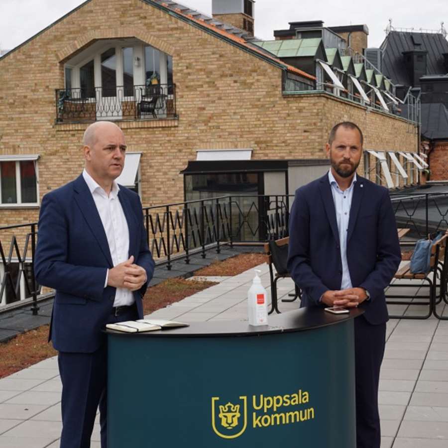 Fredrik Reinfeldt och Erik Pelling vid ett podium med Uppsala kommuns logga på.
