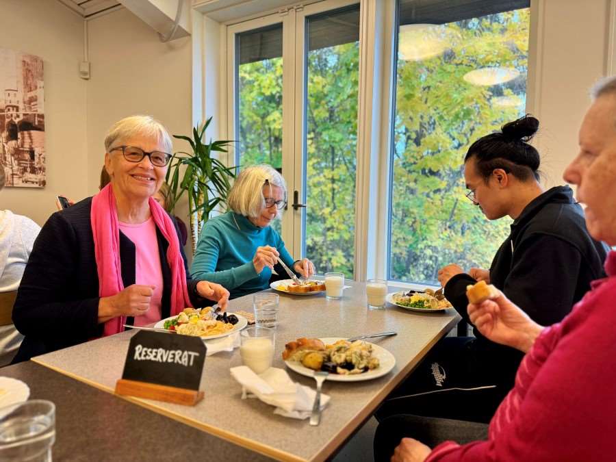 Seniorer äter lunch tillsammans i skolmatsal.